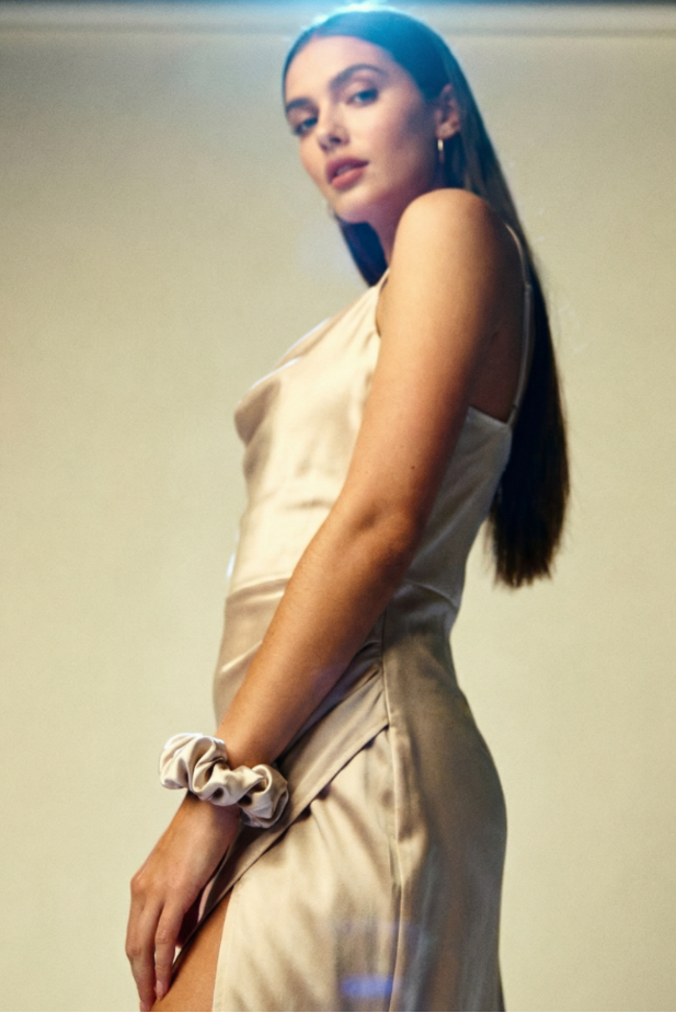 Woman in a beige dress standing against a plain background